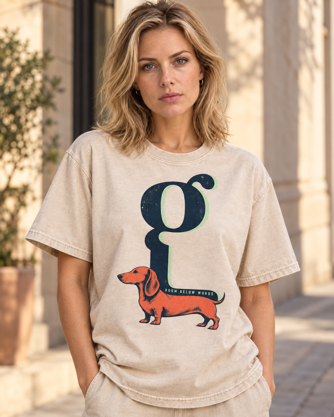 Adult model wears Apricot Dachshund Room Below Words Lowercase G washed T-shirt in a three-quarter street portrait