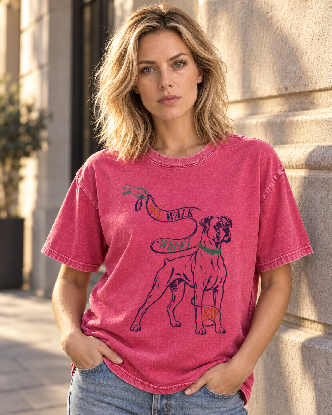 Adult model wears Fuchsia Boxer We Walk When I Say Leash washed T-shirt in a three-quarter street portrait