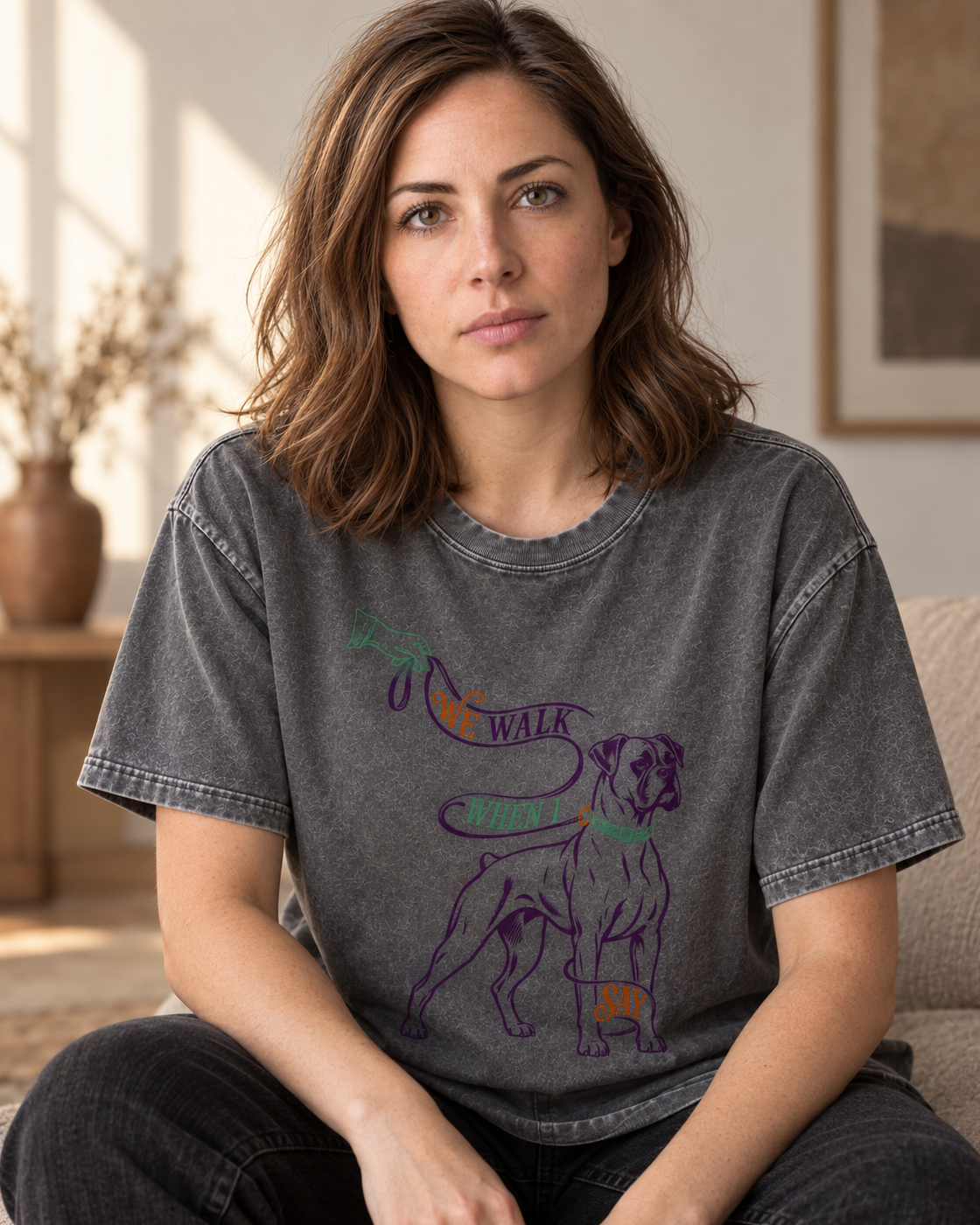 Adult model wears Gray Boxer We Walk When I Say Leash washed T-shirt in a seated indoor portrait