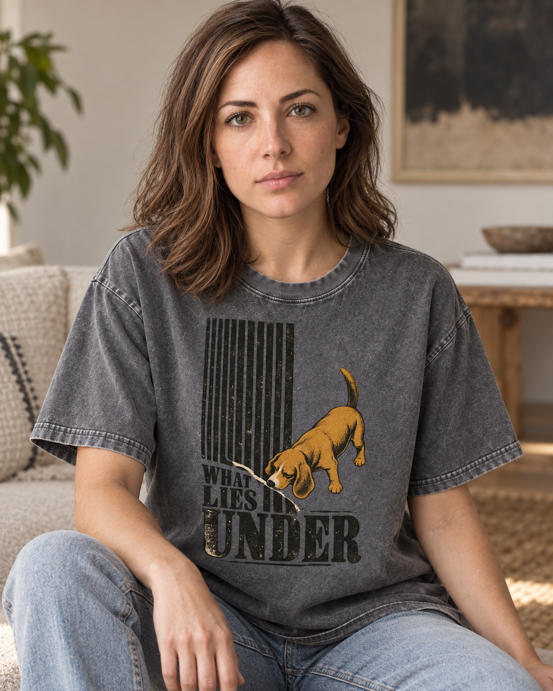 Adult model wears Gray Beagle Curious What Lies Under washed T-shirt in a seated indoor portrait