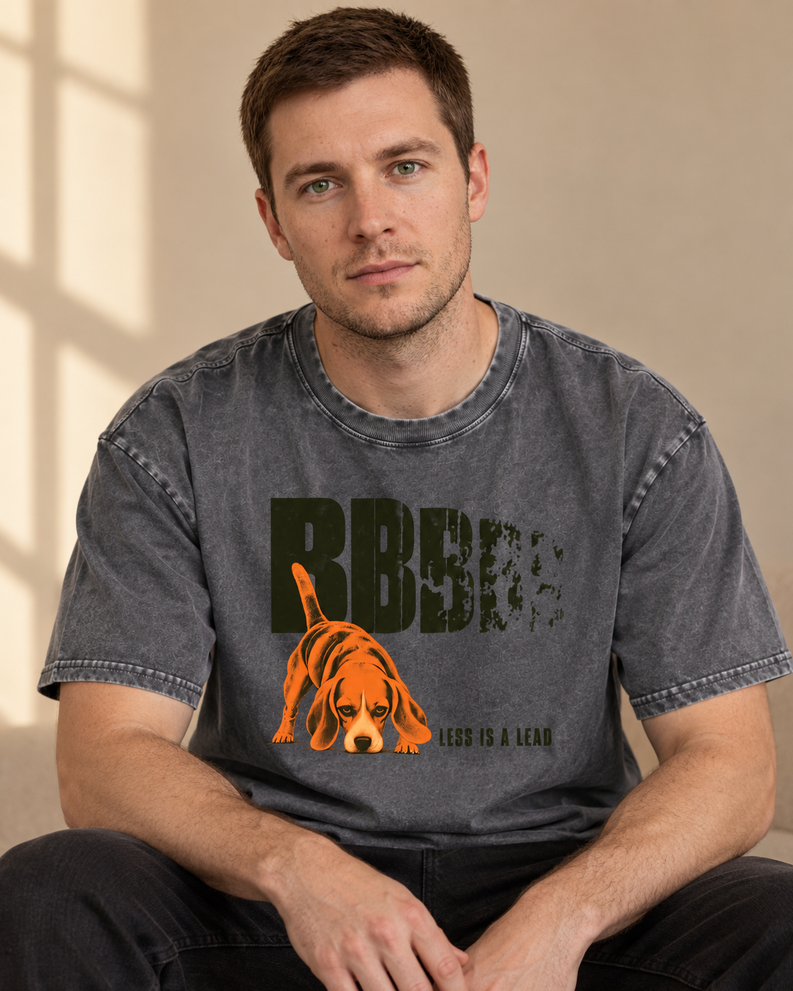 Adult model wears Gray Beagle Less Is A Lead Tracking Dog washed T-shirt in a seated indoor portrait