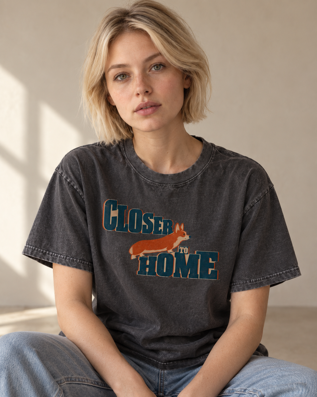 Adult model wears Gray Corgi Closer to Home Typographic washed T-shirt in a seated indoor portrait