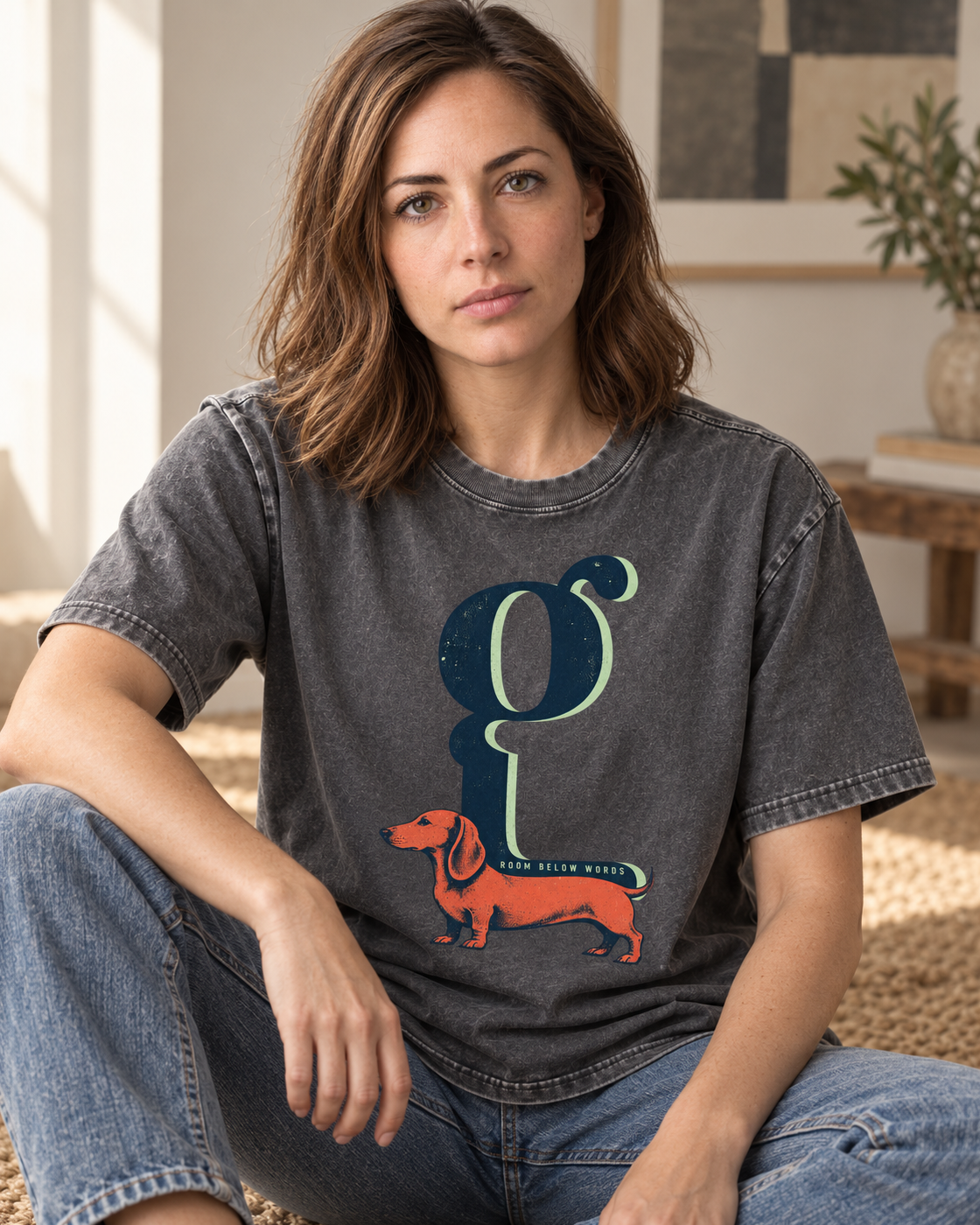 Adult model wears Gray Dachshund Room Below Words Lowercase G washed T-shirt in a seated indoor portrait