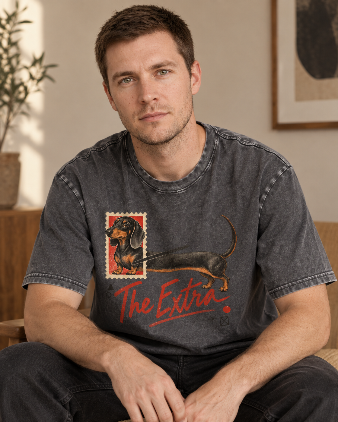 Adult model wears Gray Dachshund The Extra Postage washed T-shirt in a seated indoor portrait