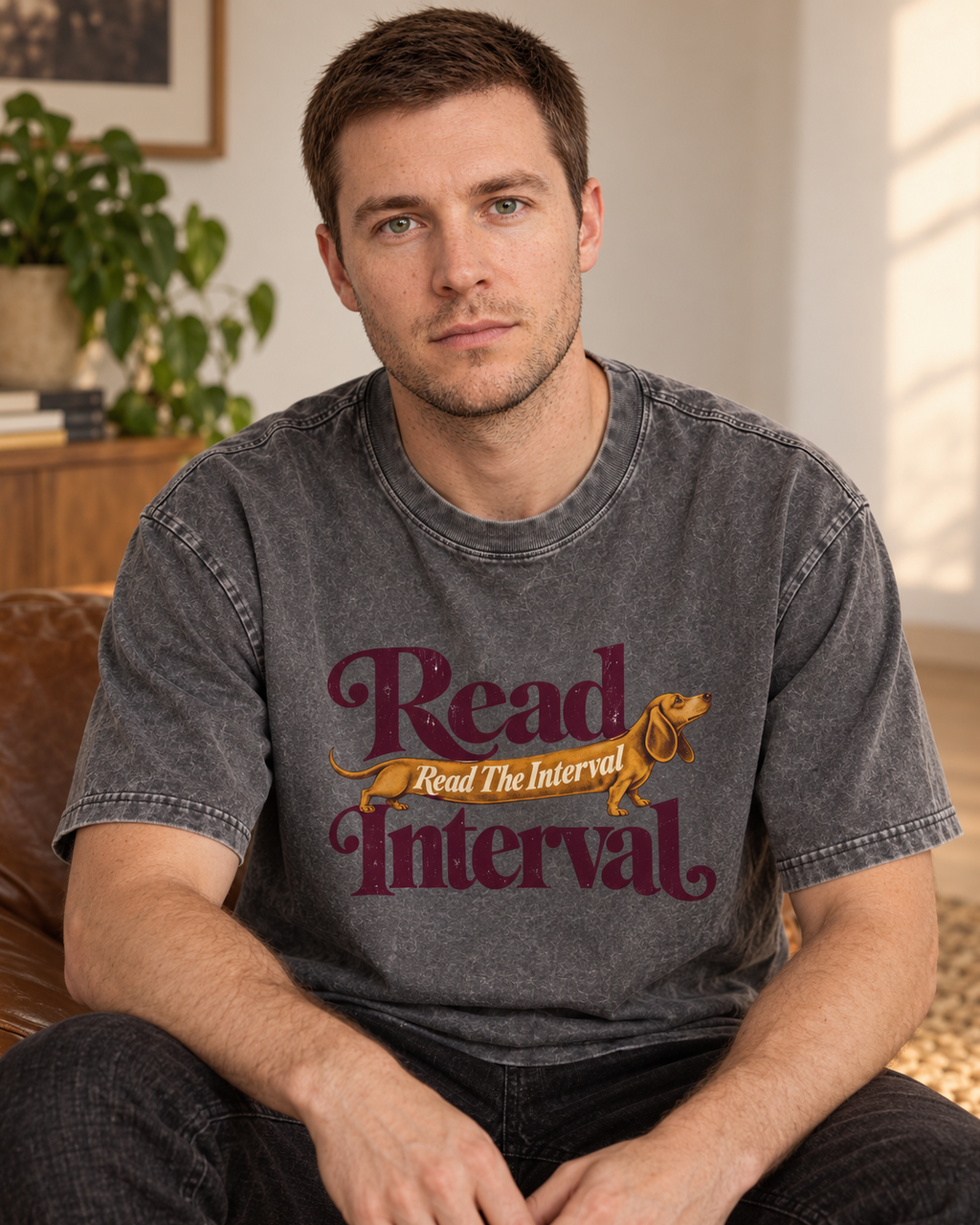 Adult model wears Gray Dachshund Read The Interval Typographic washed T-shirt in a seated indoor portrait