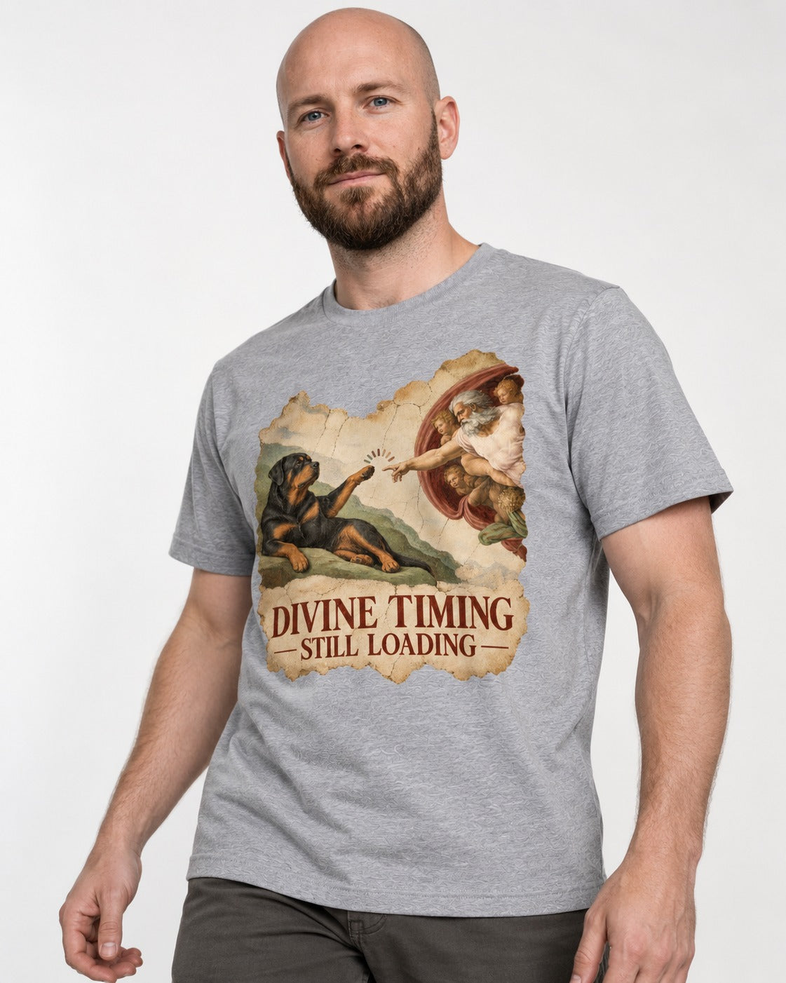 Rottweiler Divine Timing Still Loading Creation Parody Graphic T-Shirt in Sport Grey, worn by a model