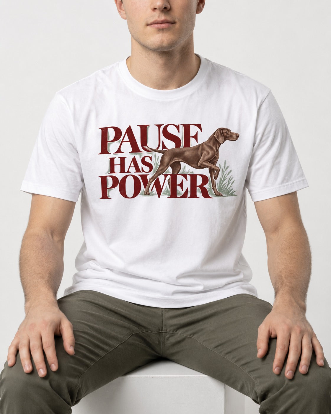 Pause Has Power German Shorthaired Pointer T-Shirt in White, worn by a seated model