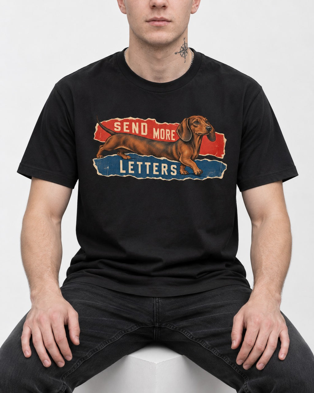 Dachshund Send More Letters Torn Paper Graphic T-Shirt in Black, worn by a seated model