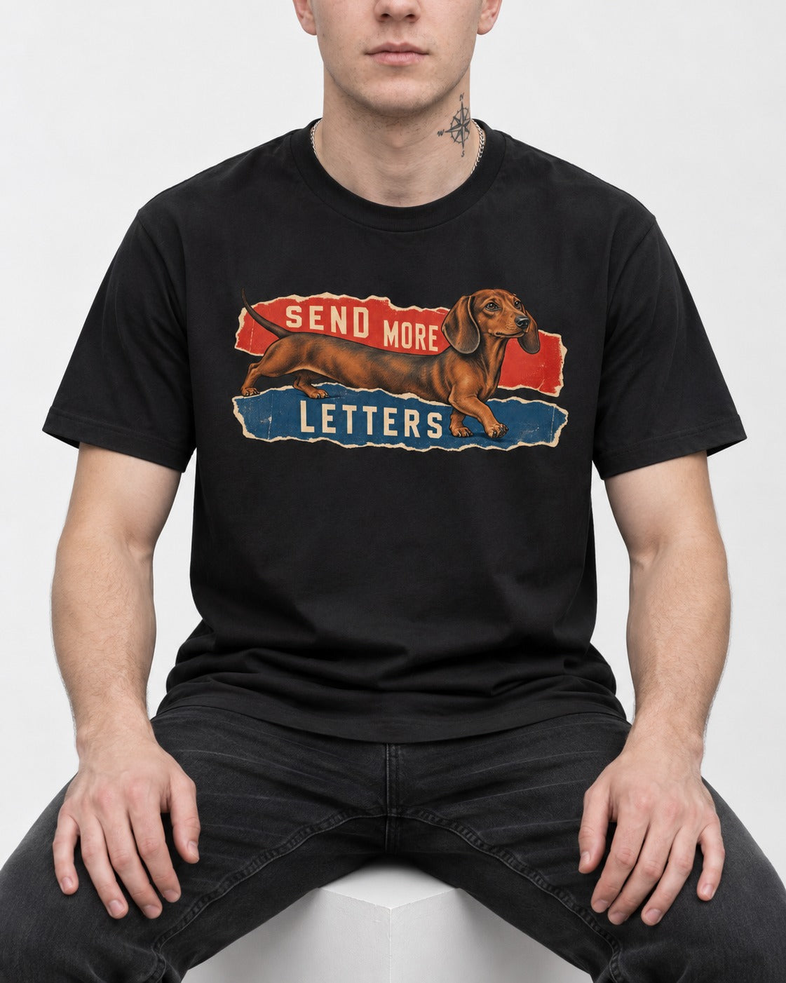 Dachshund Send More Letters Torn Paper Graphic T-Shirt in Black, worn by a seated model