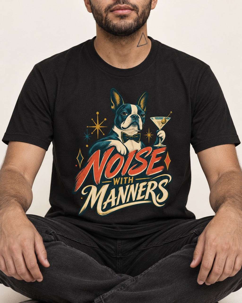 Boston Terrier Noise With Manners Cocktail Graphic T-Shirt in Black, worn by a seated model