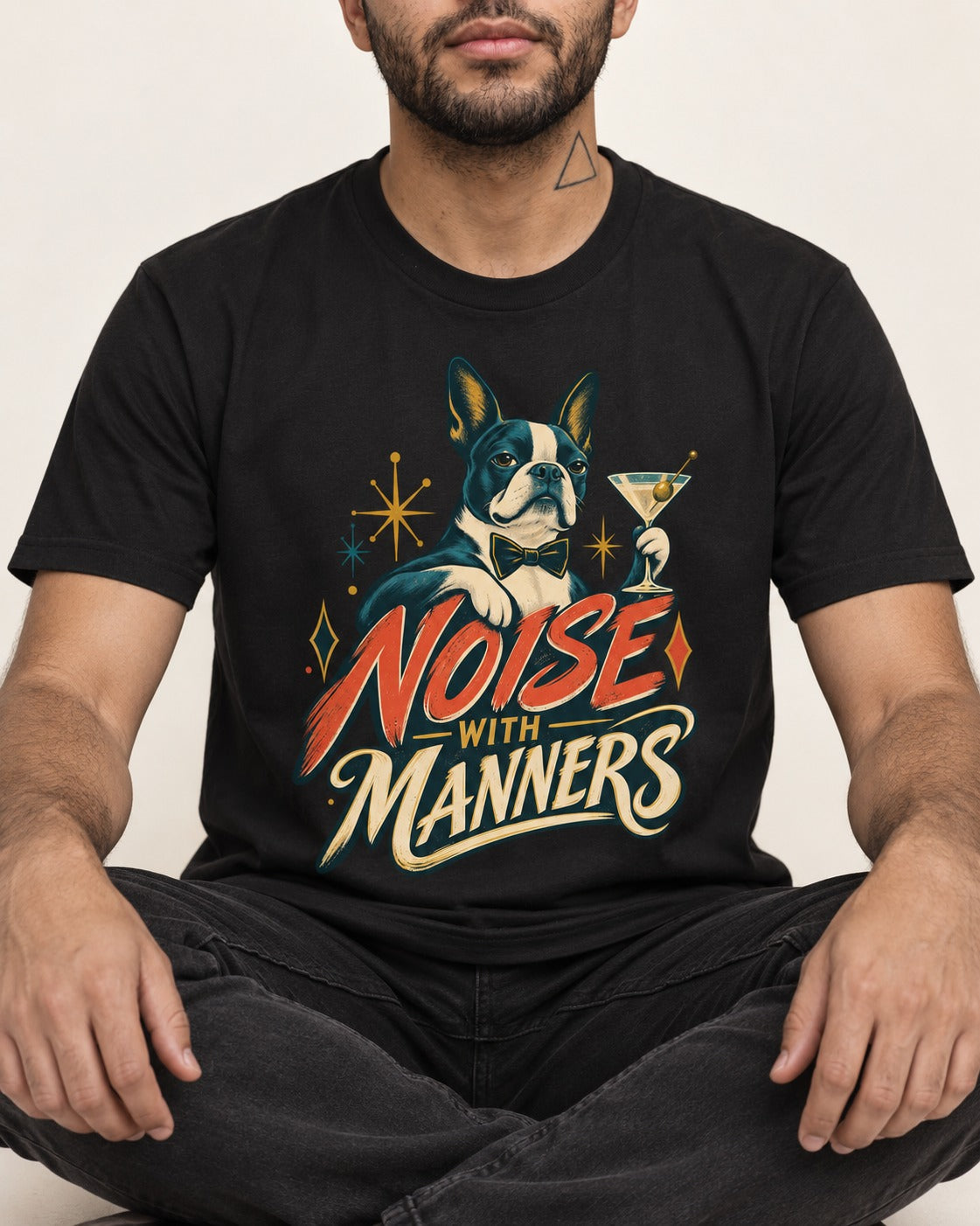 Boston Terrier Noise With Manners Cocktail Graphic T-Shirt in Black, worn by a seated model
