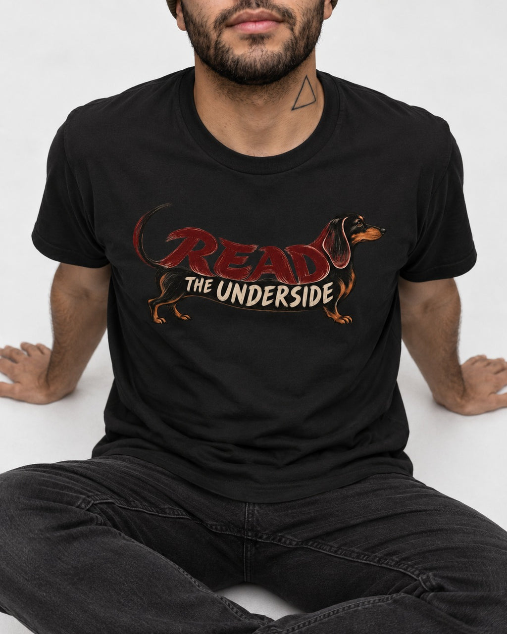 Dachshund Read The Underside Body Lettering Graphic T-Shirt in Black, worn by a seated model