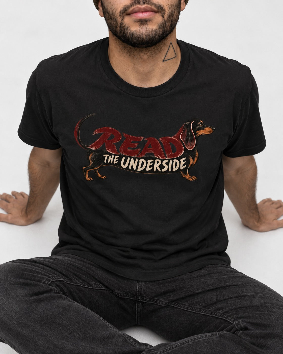Dachshund Read The Underside Body Lettering Graphic T-Shirt in Black, worn by a seated model