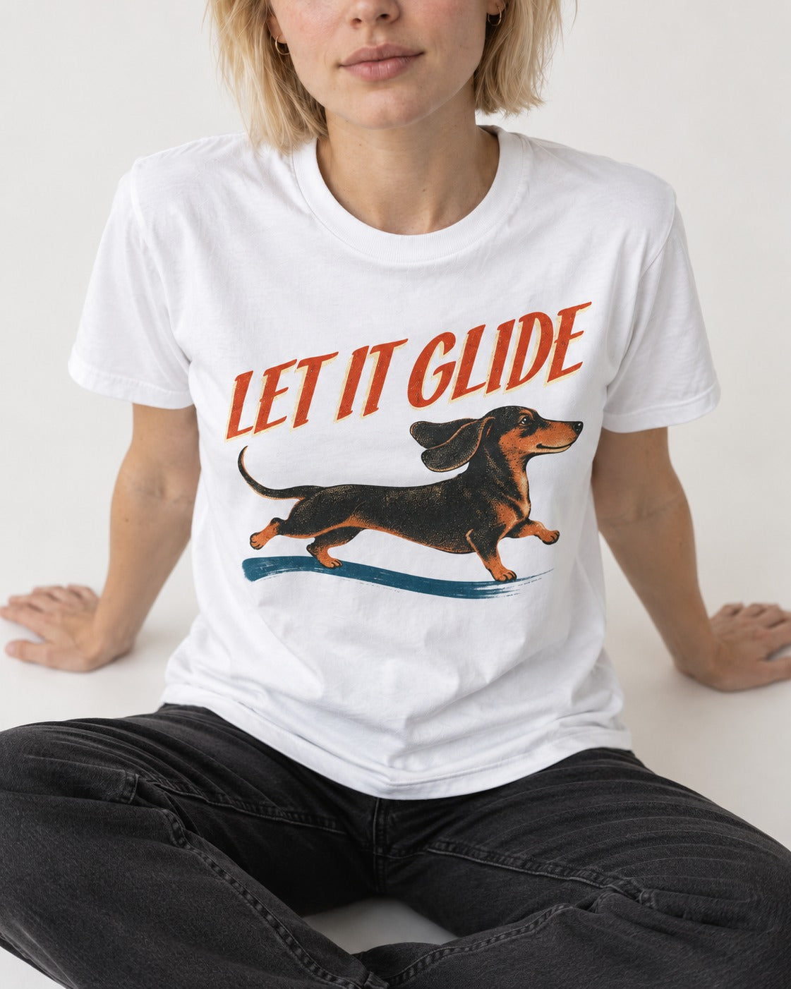 Let It Glide Dachshund T-Shirt in White, worn by a seated model
