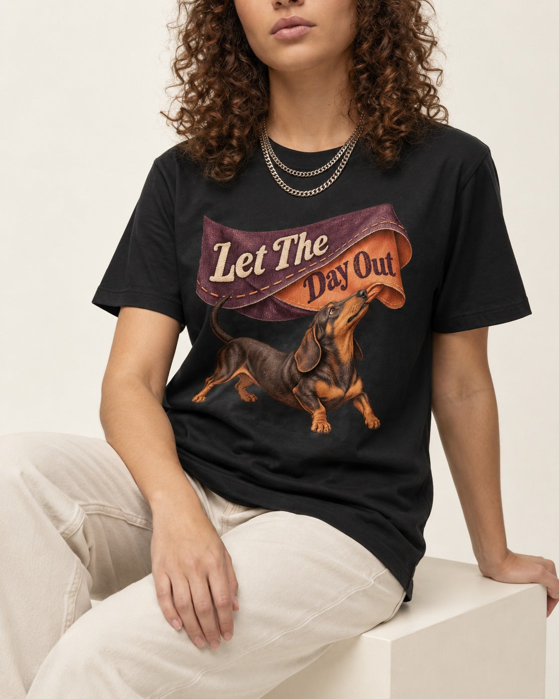Dachshund Let The Day Out Fabric Banner Graphic T-Shirt in Black, worn by a seated model