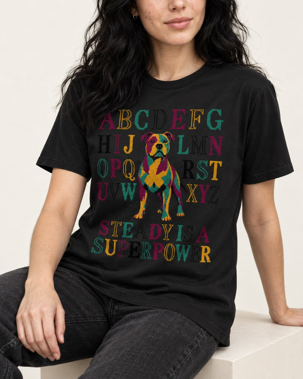 Pitbull Steady Is a Superpower Alphabet Graphic T-Shirt in Black, worn by a seated model