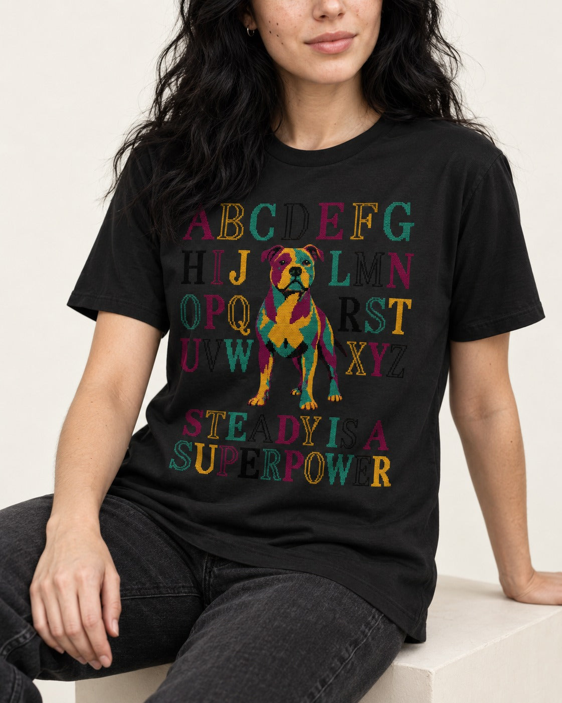 Pitbull Steady Is a Superpower Alphabet Graphic T-Shirt in Black, worn by a seated model