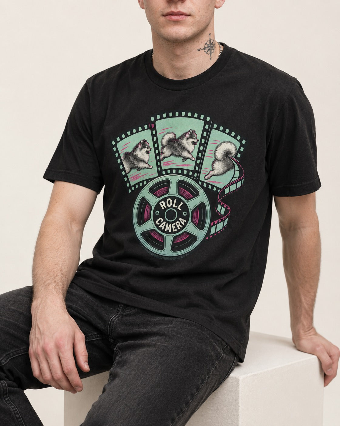 Pomeranian Roll Camera Film Reel Graphic T-Shirt in Black, worn by a seated model
