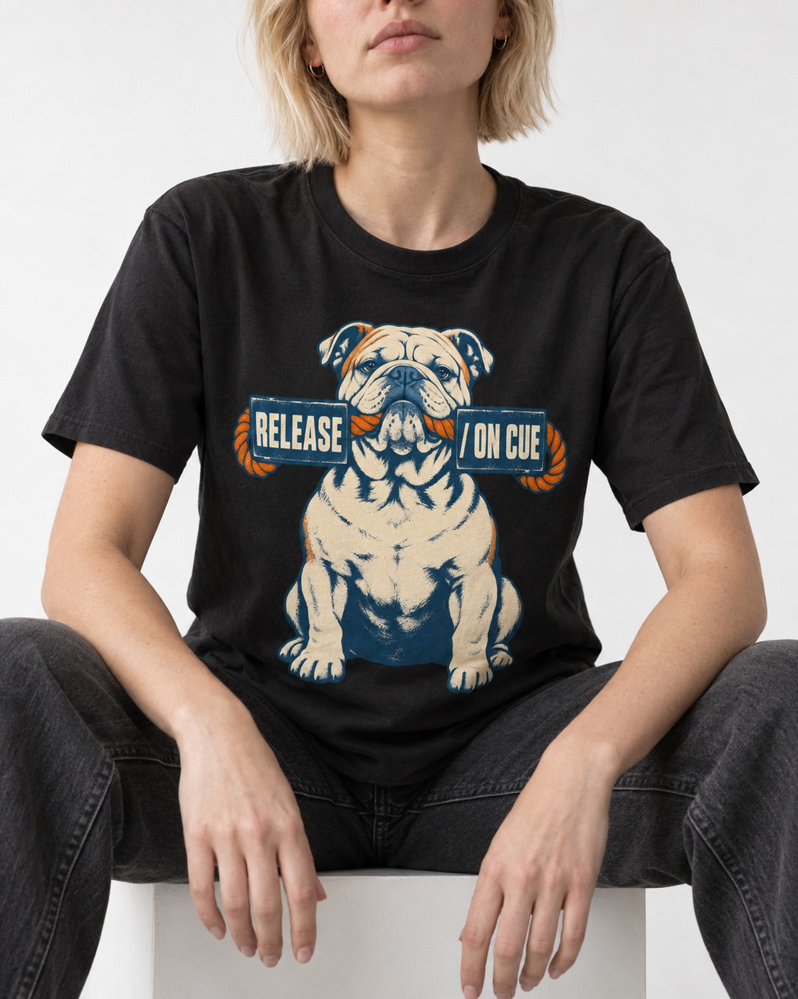 English Bulldog Release on Cue Rope Sign Graphic T-Shirt in Black, worn by a seated model
