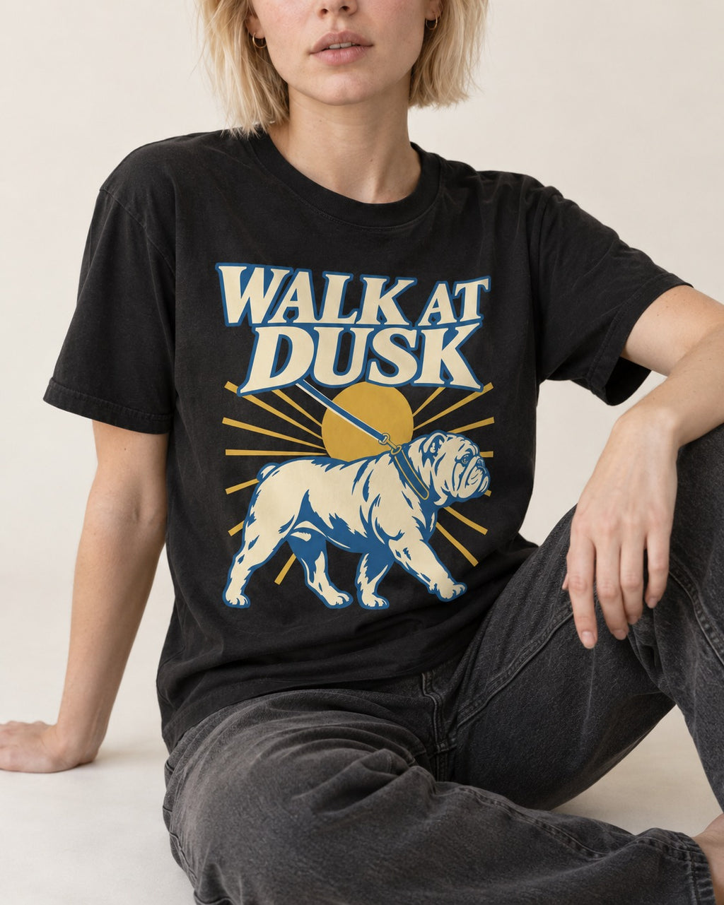 English Bulldog Walk at Dusk Sunset Graphic T-Shirt in Black, worn by a seated model