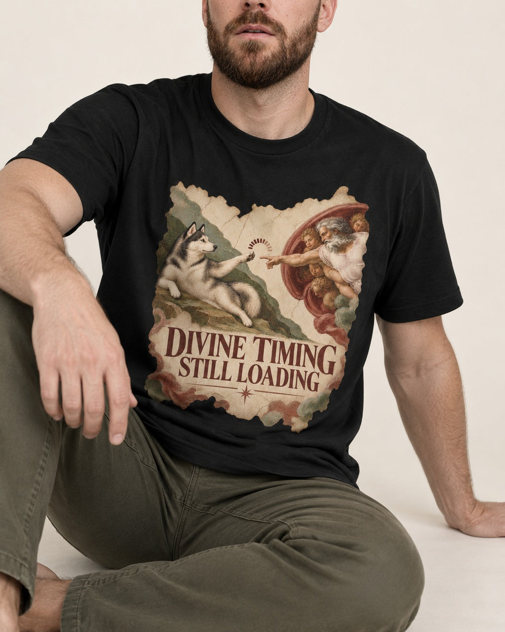Husky Divine Timing Still Loading Creation Parody Graphic T-Shirt in Black, worn by a seated model