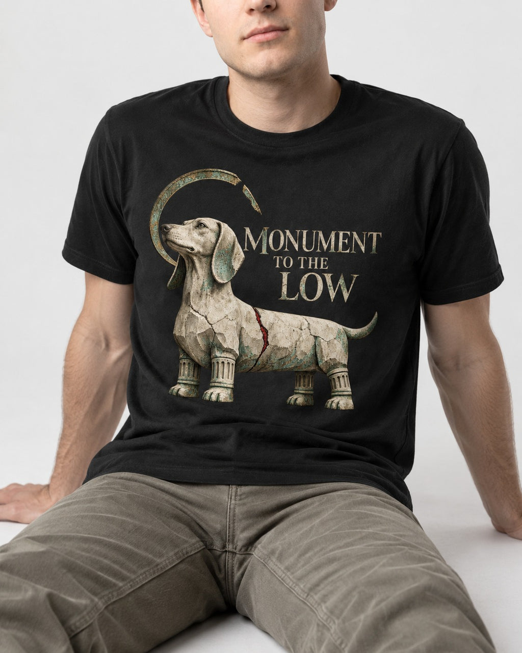 Dachshund Monument to the Low Stone Statue Graphic T-Shirt in Black, worn by a seated model