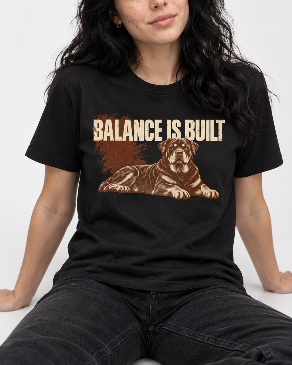 Rottweiler Balance Is Built Resting Strength Graphic T-Shirt in Black, worn by a seated model