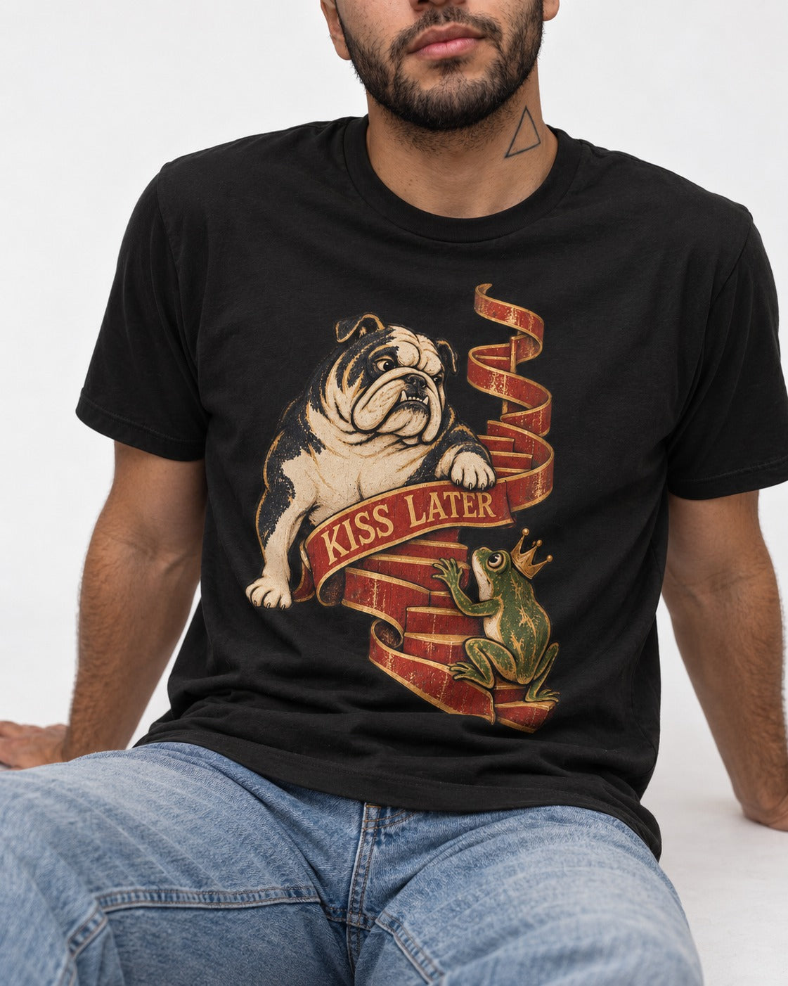 English Bulldog Kiss Later Frog Prince Graphic T-Shirt in Black, worn by a seated model