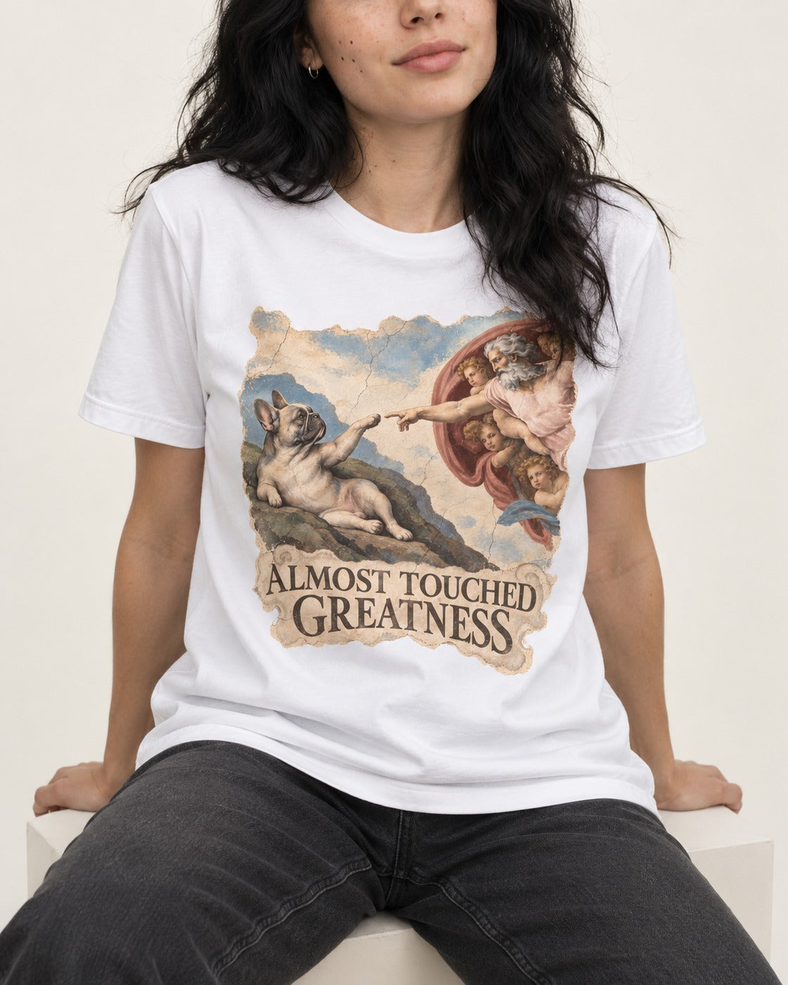 Frenchie Almost Touched Greatness T-Shirt in White, worn by a seated model