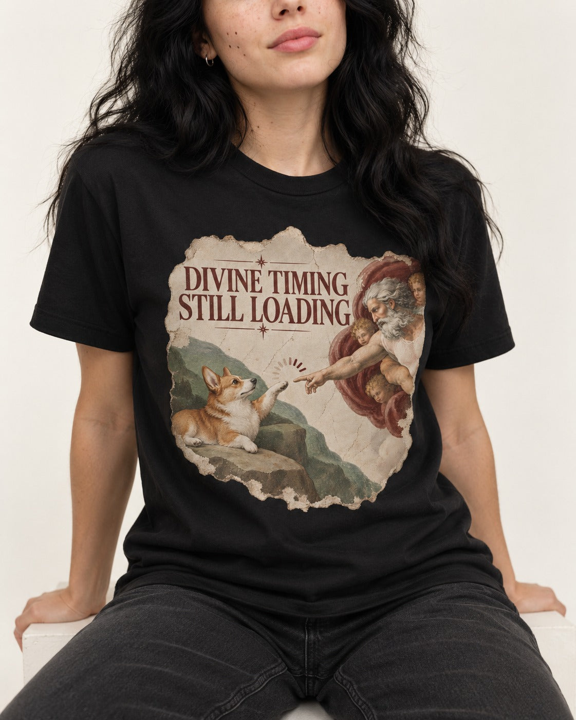 Corgi Divine Timing Still Loading Creation Parody T-Shirt in Black, worn by a seated model