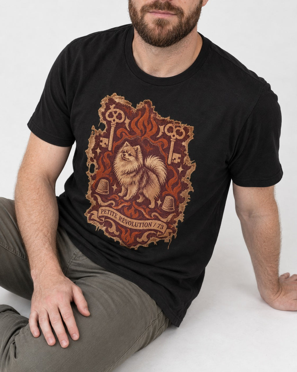 Pomeranian Petite Revolution Ornate Key Emblem Graphic T-Shirt in Black, worn by a seated model