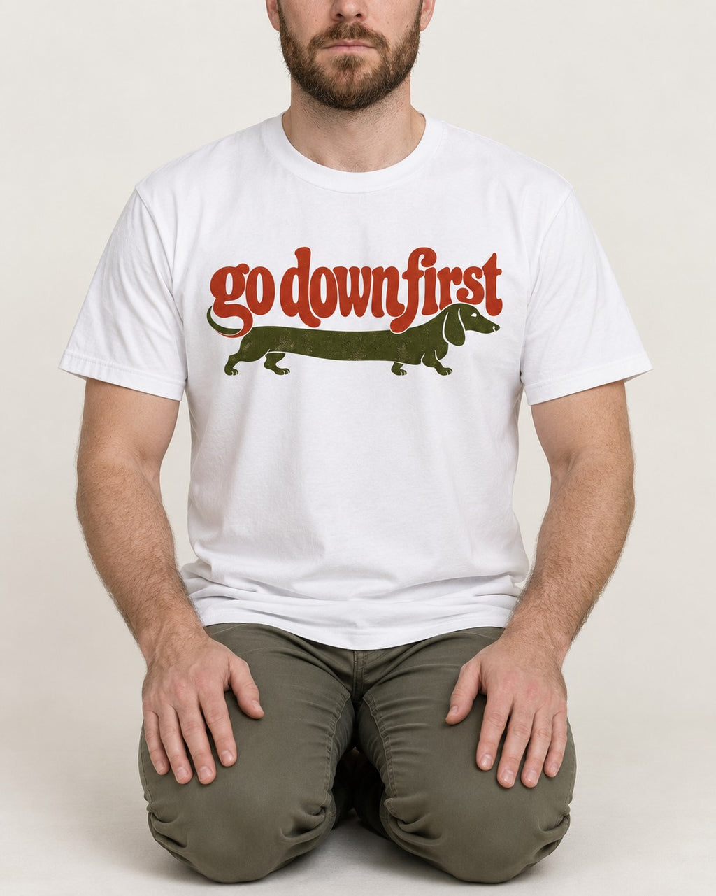Dachshund Goes Down First T-Shirt in White, worn by a seated model