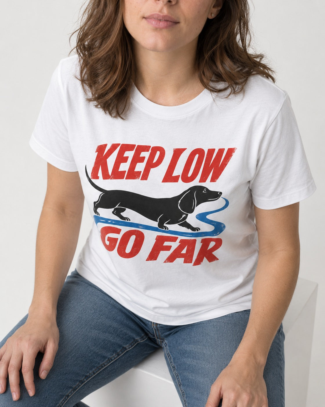 Keep Low Go Far Dachshund T-Shirt in White, worn by a seated model