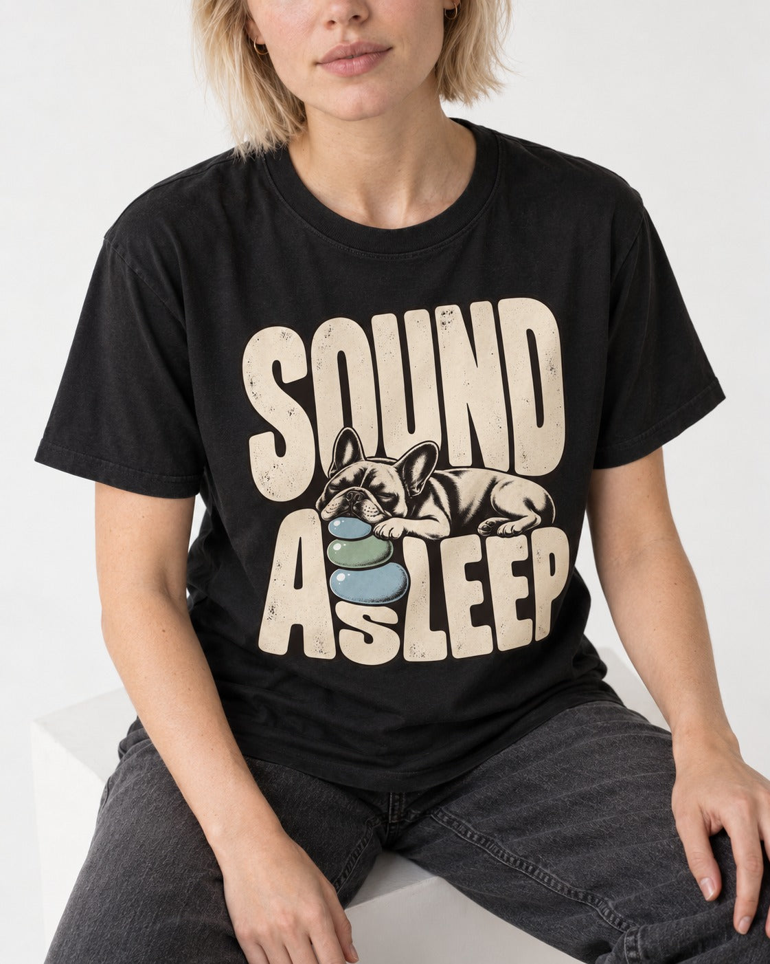 Frenchie Sound Asleep Stone Pillow Graphic T-Shirt in Black, worn by a seated model