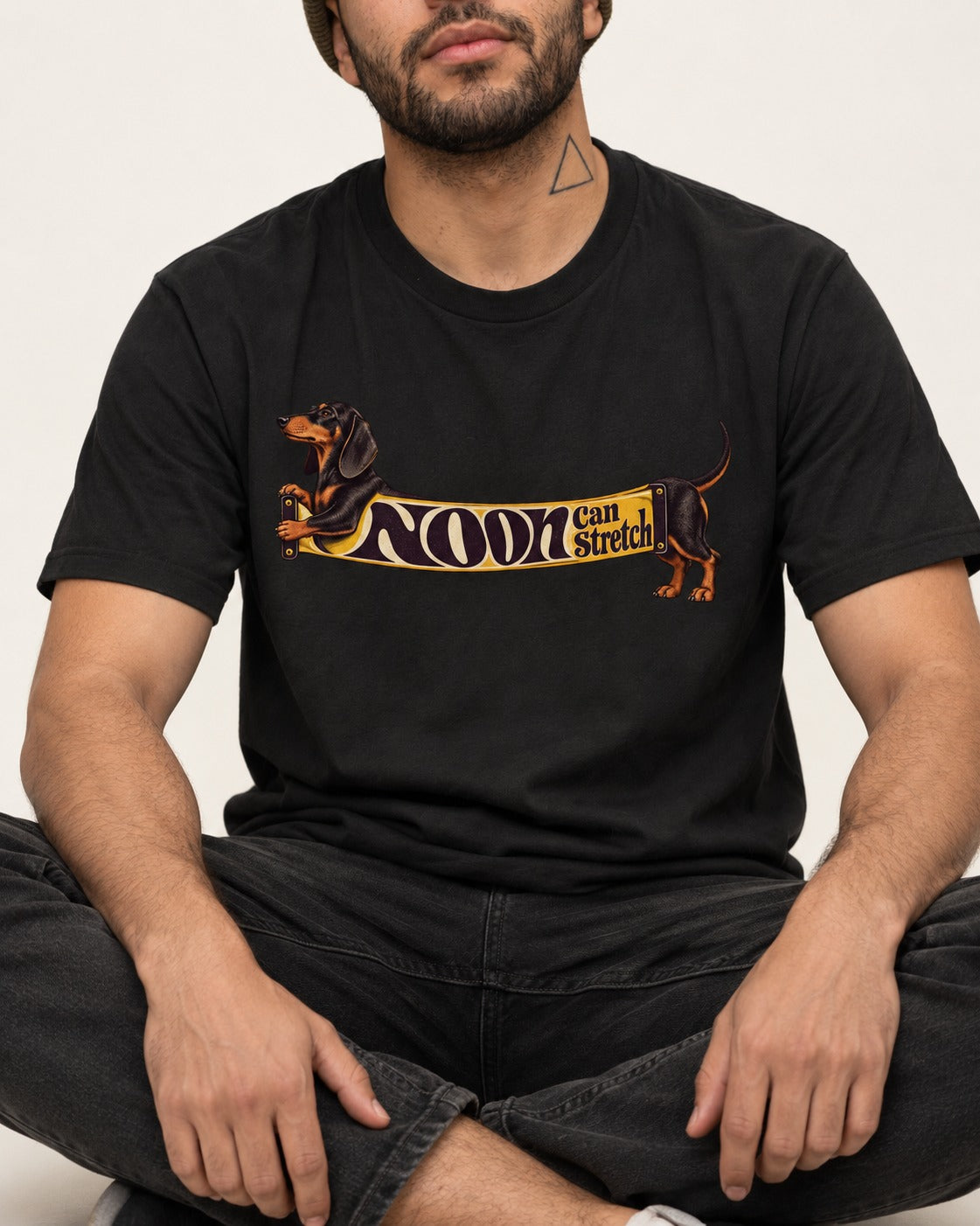 Dachshund Noon Can Stretch Sign Graphic T-Shirt in Black, worn by a seated model