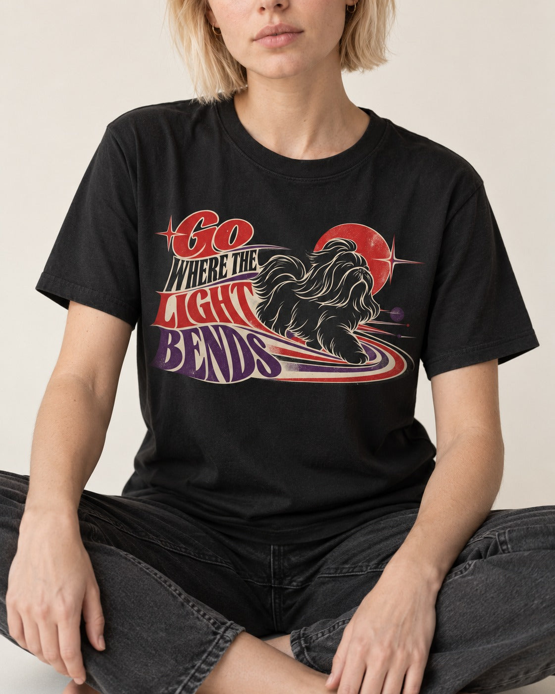 Shih Tzu Go Where the Light Bends Cosmic Orbit Graphic T-Shirt in Black, worn by a seated model