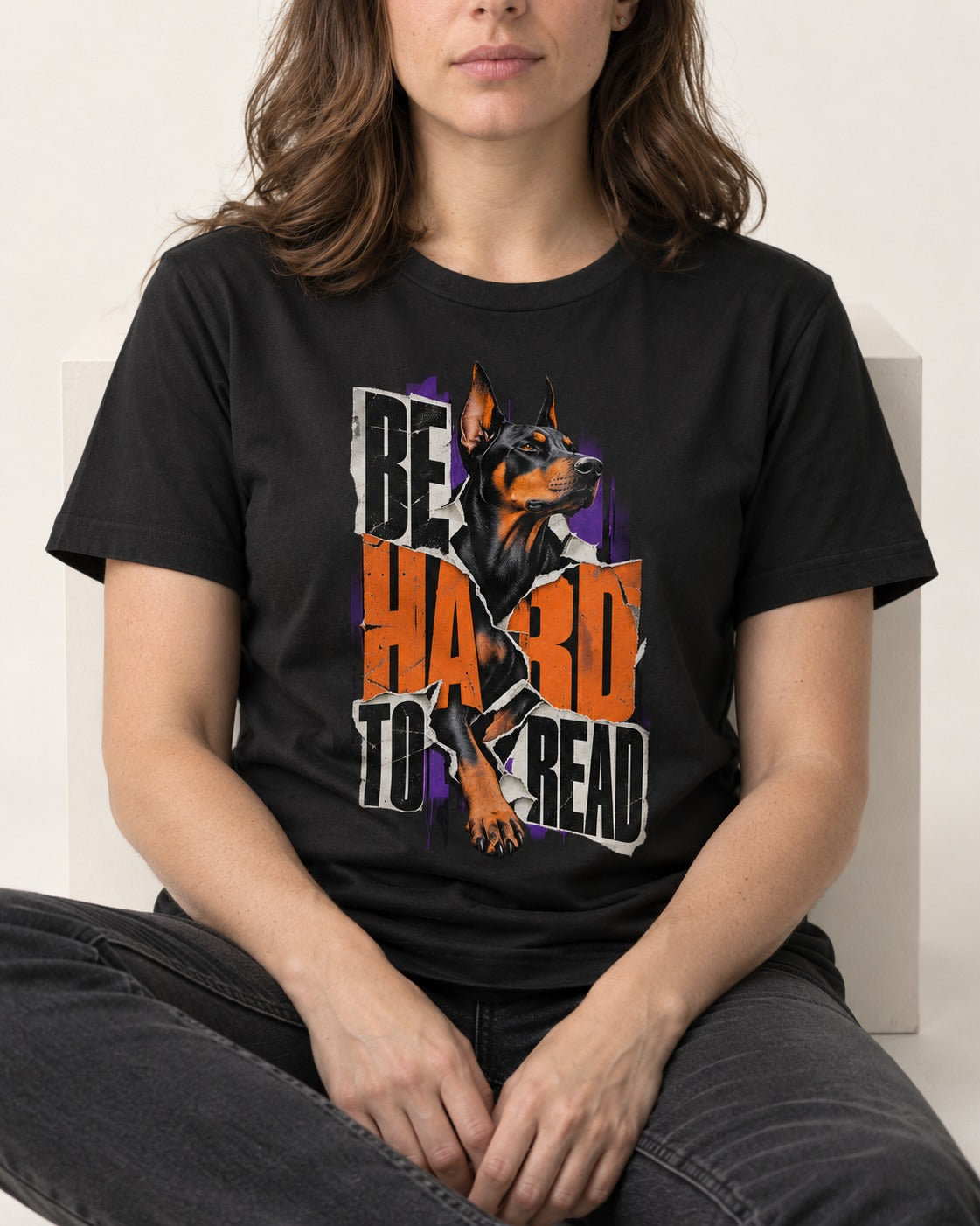 Doberman Be Hard to Read Torn Poster Graphic T-Shirt in Black, worn by a seated model