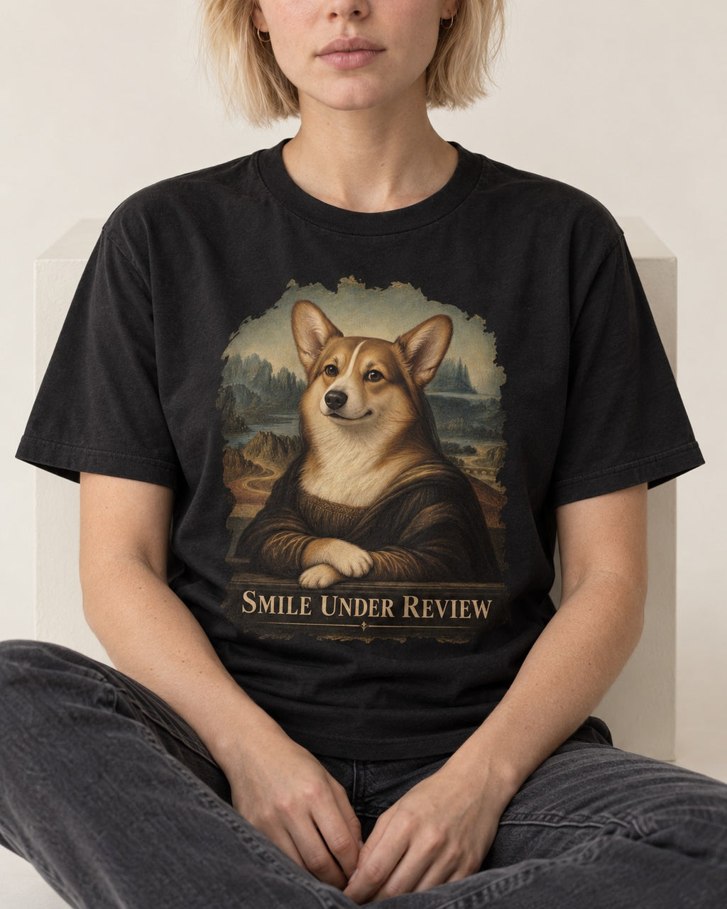 Corgi Smile Under Review Mona Lisa Portrait T-Shirt in Black, worn by a seated model