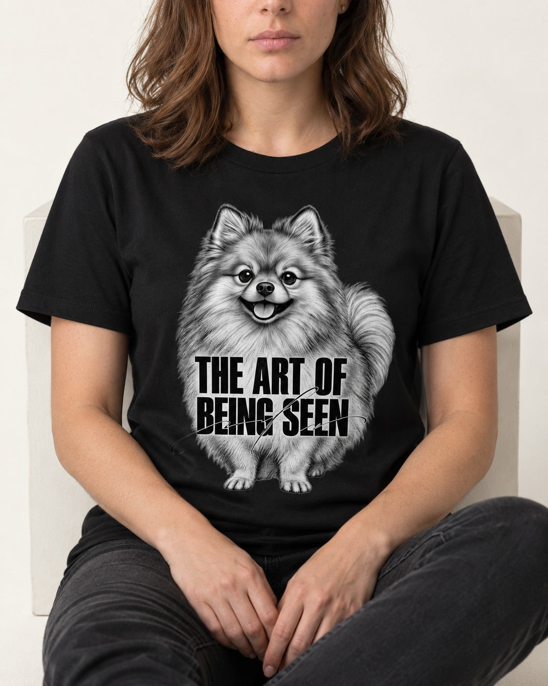 Pomeranian The Art of Being Seen Portrait Graphic T-Shirt in Black, worn by a seated model
