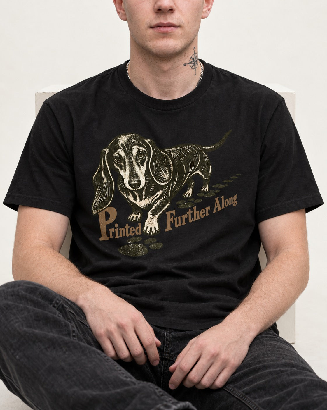 Dachshund Printed Further Along Footprint Graphic T-Shirt in Black, worn by a seated model