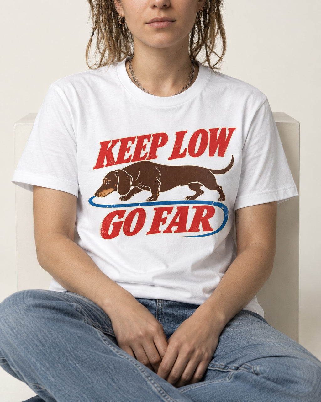 Dachshund Keep Low Go Far T-Shirt in White, worn by a seated model