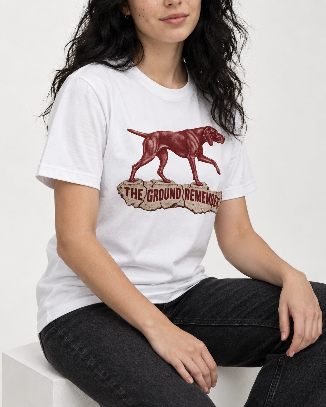 The Ground Remembers German Shorthaired Pointer T-Shirt in White, worn by a seated model