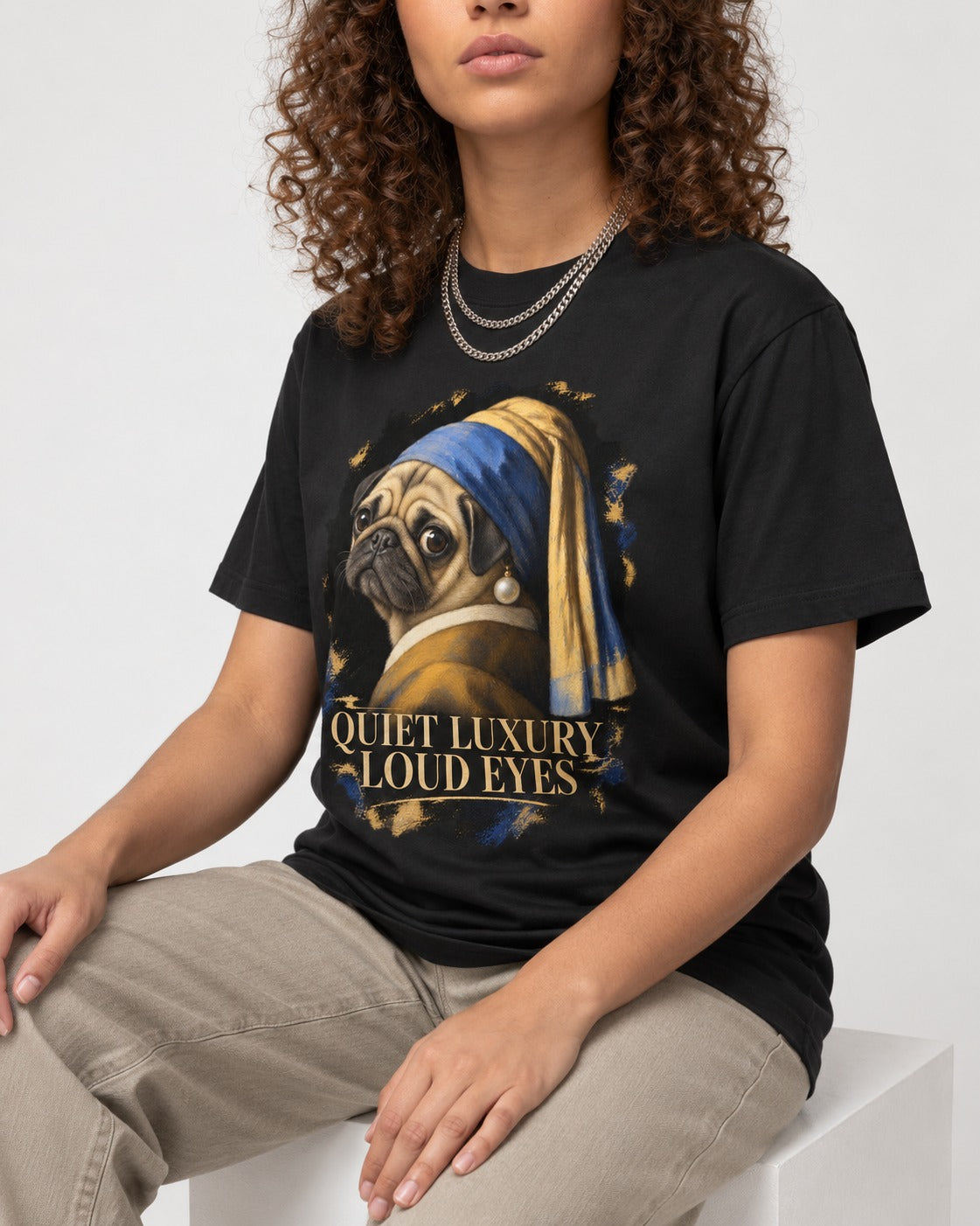 Pug Quiet Luxury Loud Eyes Pearl Portrait Graphic T-Shirt in Black, worn by a seated model