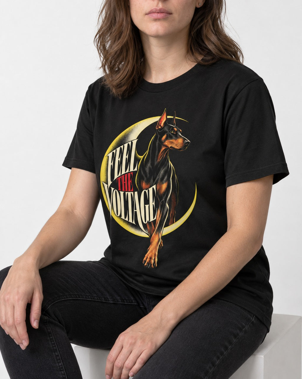 Doberman Feel the Voltage Crescent Portrait Graphic T-Shirt in Black, worn by a seated model