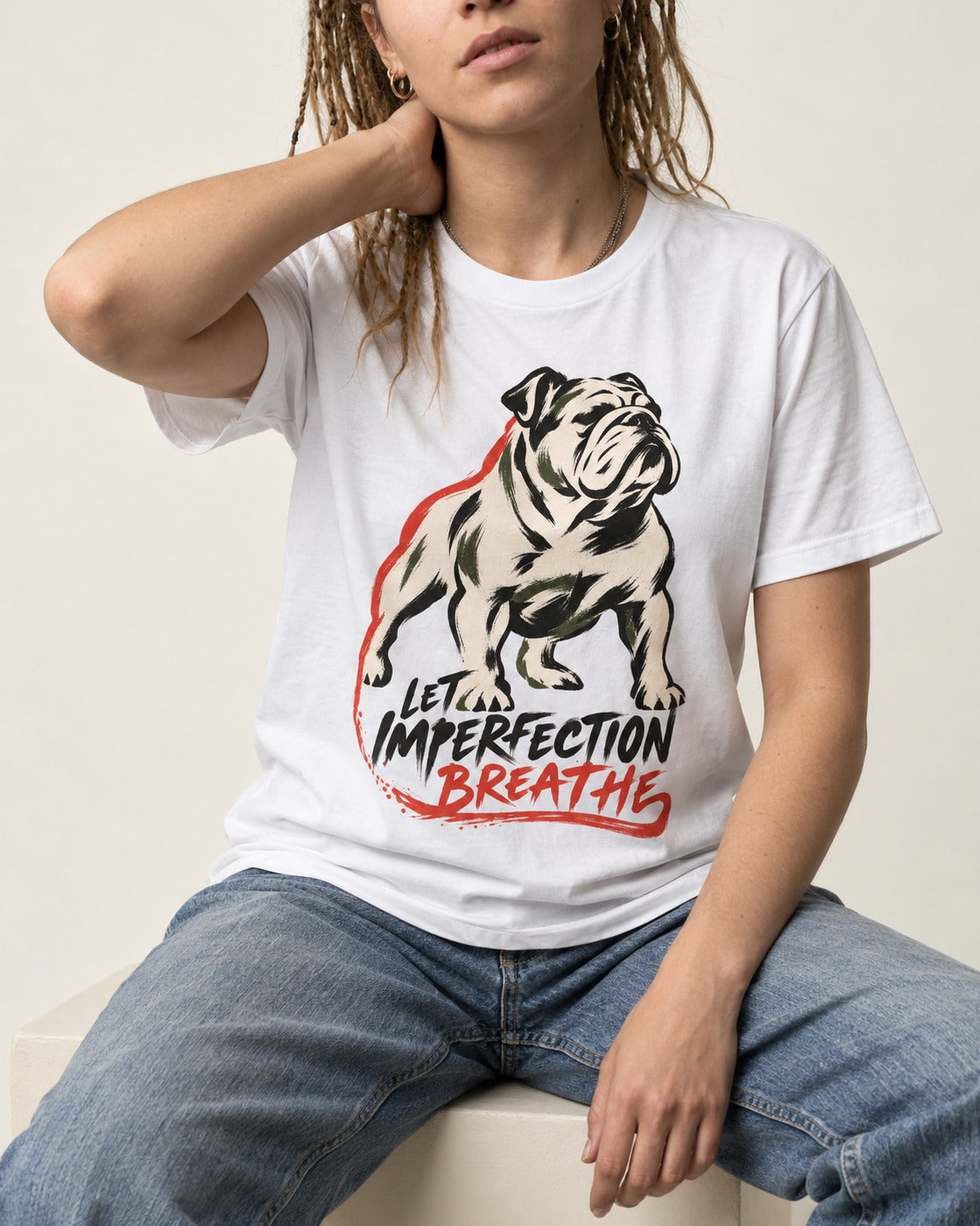 Let Imperfection Breathe English Bulldog T-Shirt in White, worn by a seated model