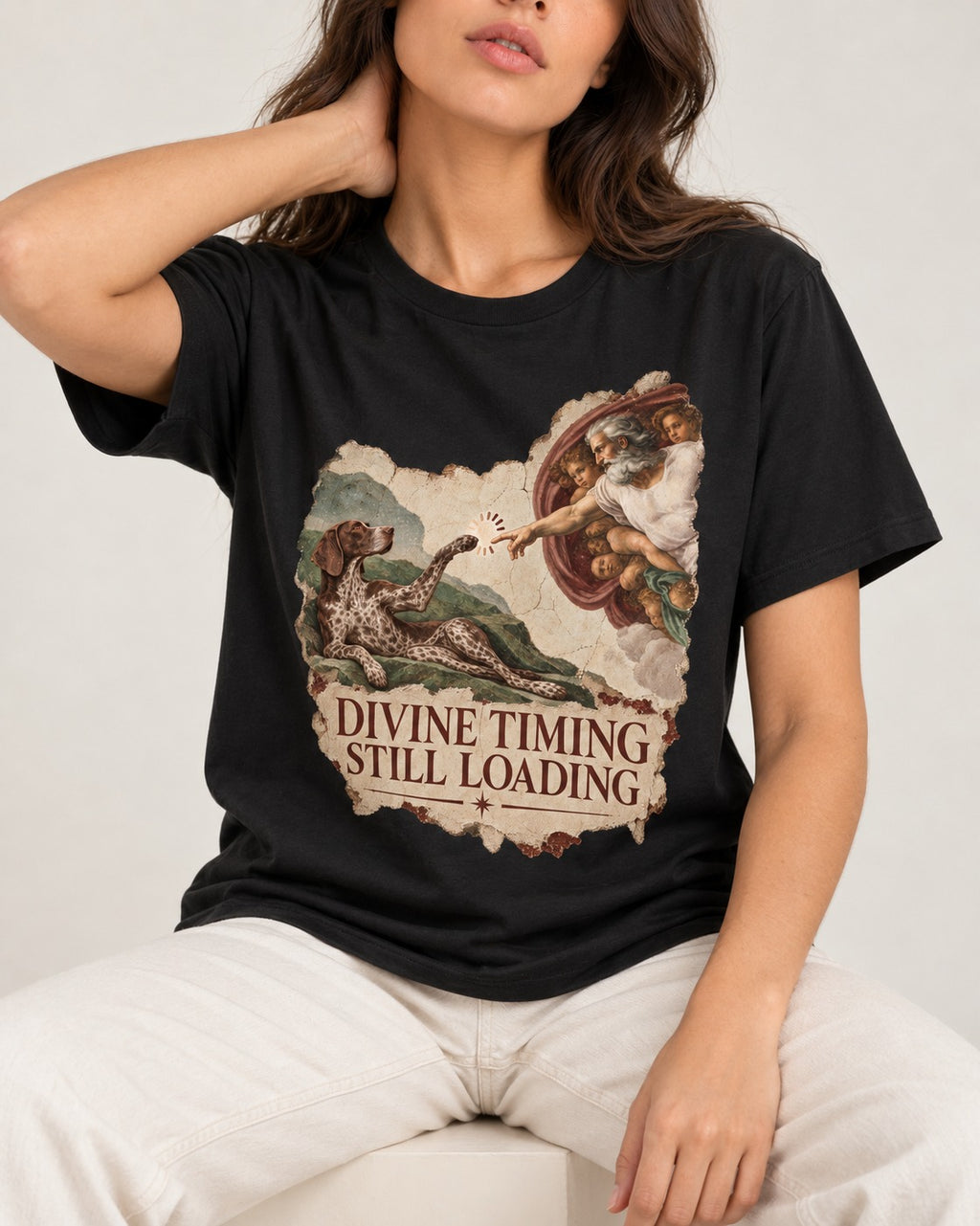 German Shorthaired Pointer Divine Timing Still Loading Creation Scene Graphic T-Shirt in Black, worn by a seated model