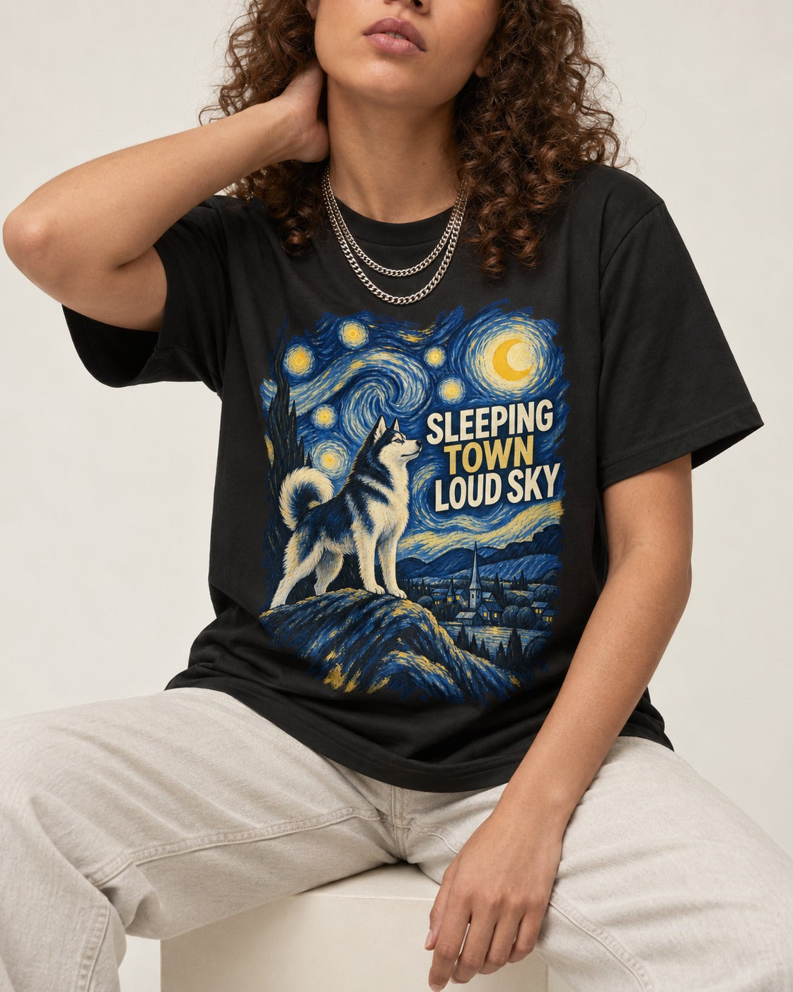Husky Sleeping Town Loud Sky Starry Night Graphic T-Shirt in Black, worn by a seated model