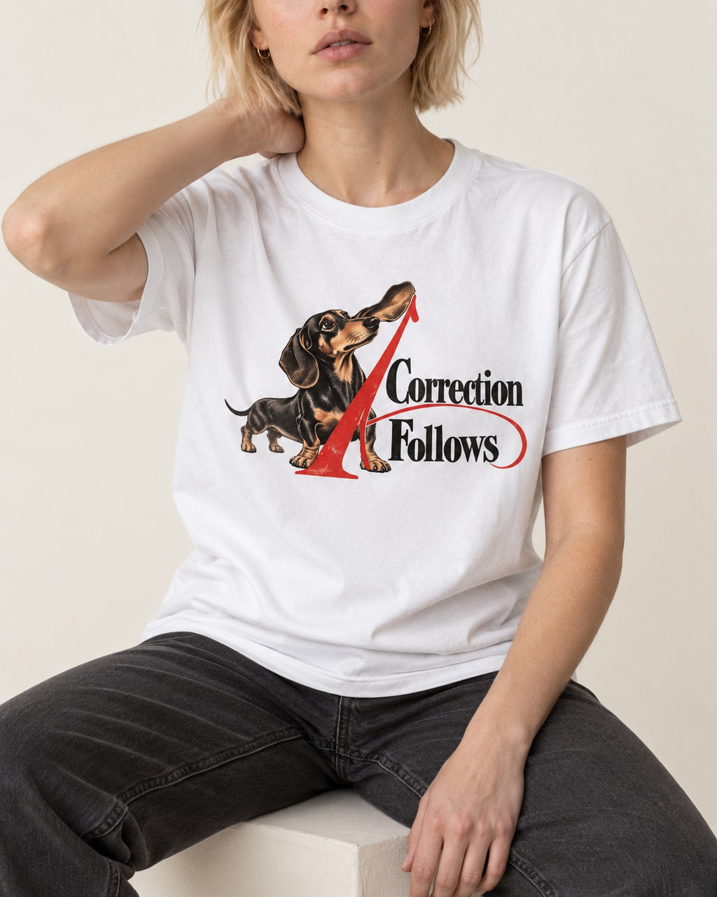 A Dachshund Correction Follows T-Shirt in White, worn by a seated model