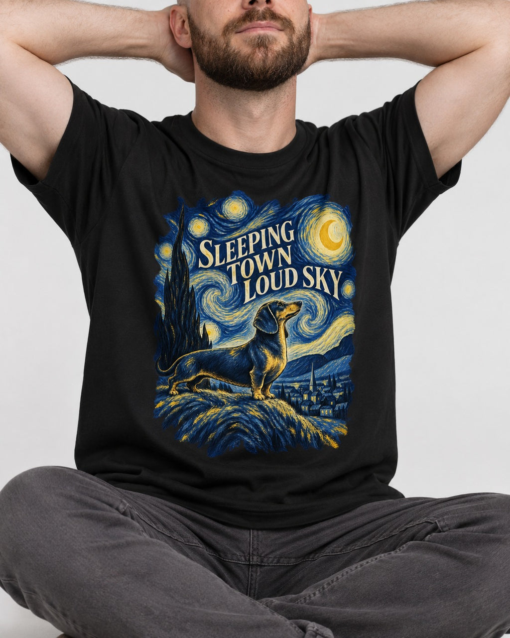 Dachshund Sleeping Town Loud Sky Starry Night Graphic T-Shirt in Black, worn by a seated model