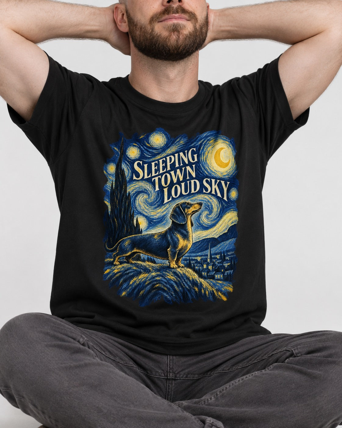Dachshund Sleeping Town Loud Sky Starry Night Graphic T-Shirt in Black, worn by a seated model